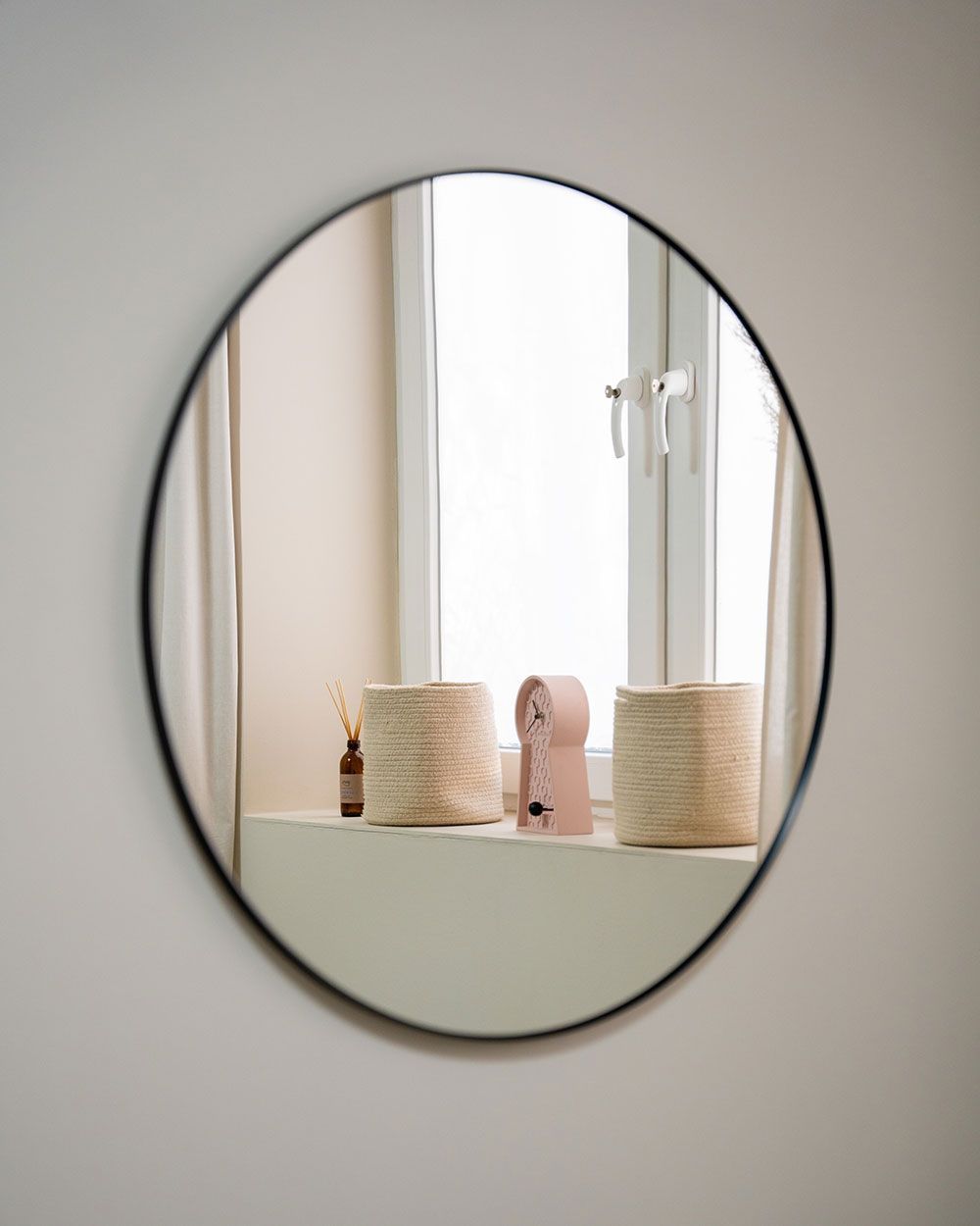 Ein runder Spiegel hängt an einer Wand neben einem Fenster