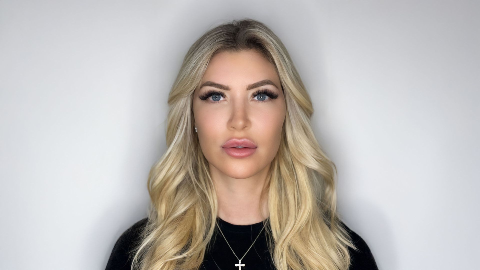 Eine Frau mit langen blonden Haaren trägt ein schwarzes Hemd und eine Halskette mit einem Kreuz.