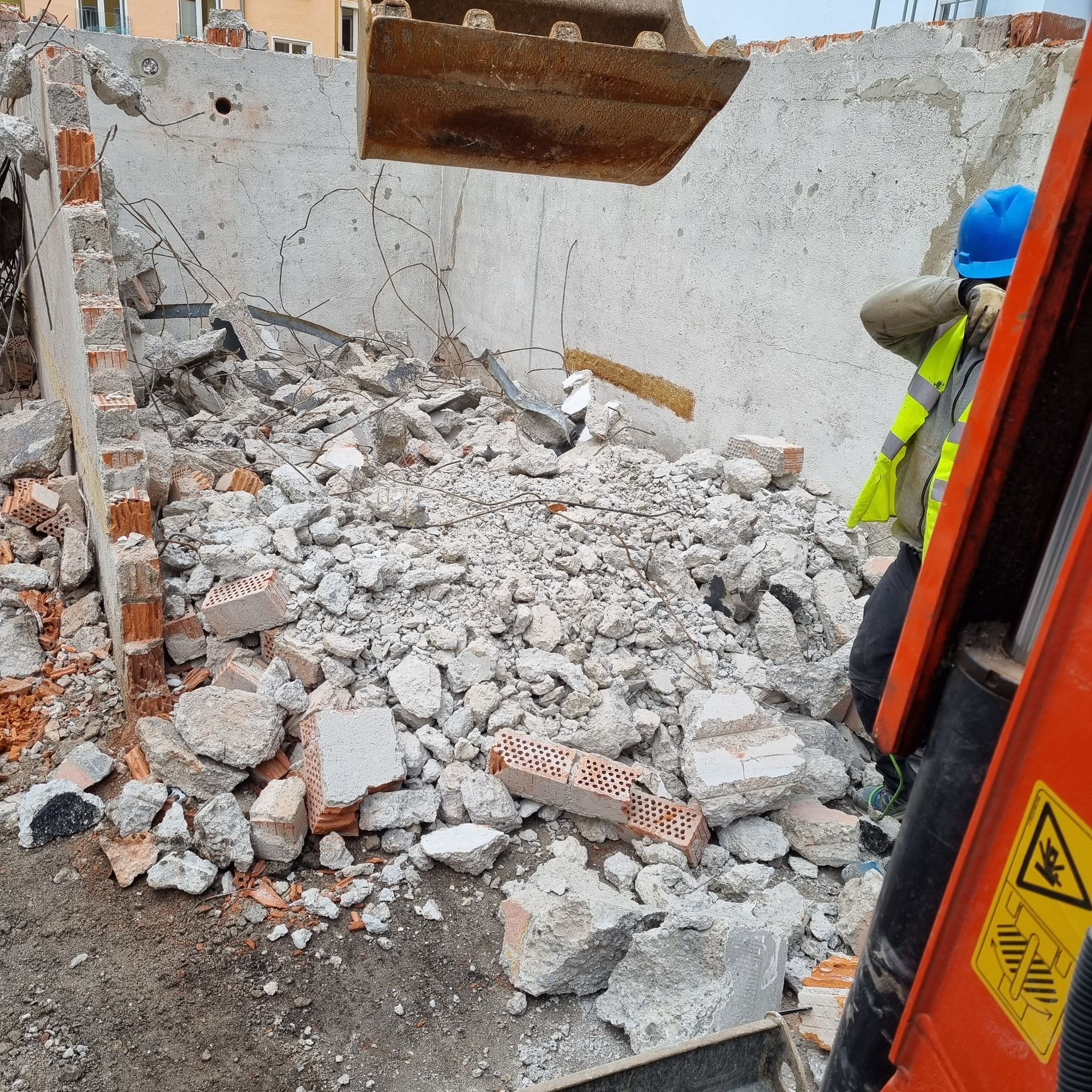 Abbruchstelle: Bagger hebt Schutt weg; Arbeiter in Sicherheitsausrüstung; Schutthaufen.