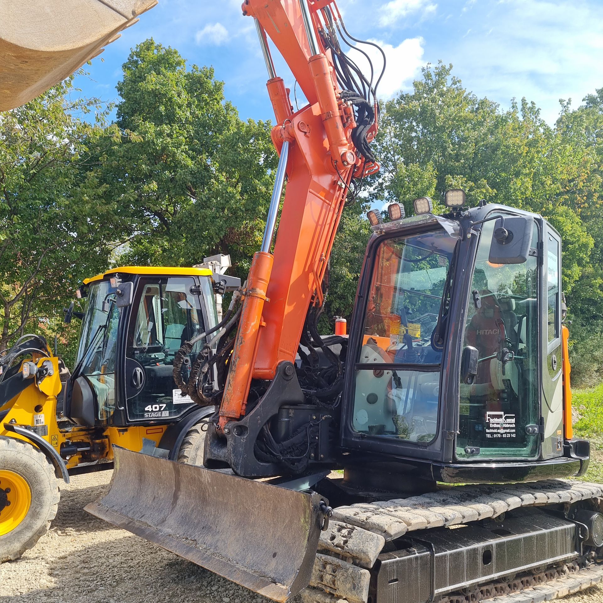 Orangefarbener Bagger mit schwarzer Kabine und Ketten, im Freien neben einem gelben Kompaktlader geparkt.