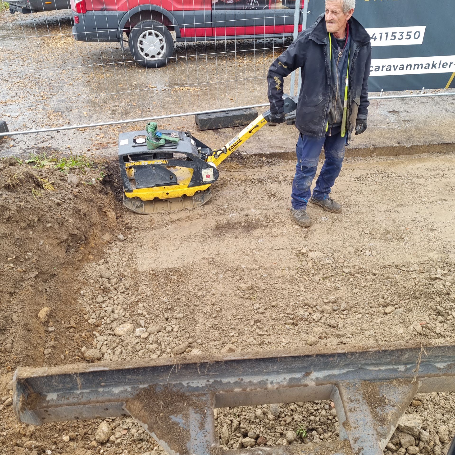 Mann bedient eine gelbe Rüttelplatte auf einer Baustelle.