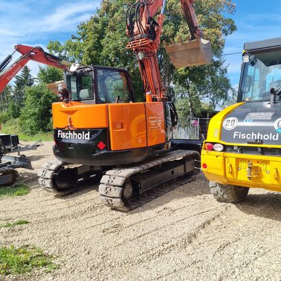 Gelber Bagger zerstört ein Gebäude, umgeben von Schutt unter einem bewölkten Himmel.