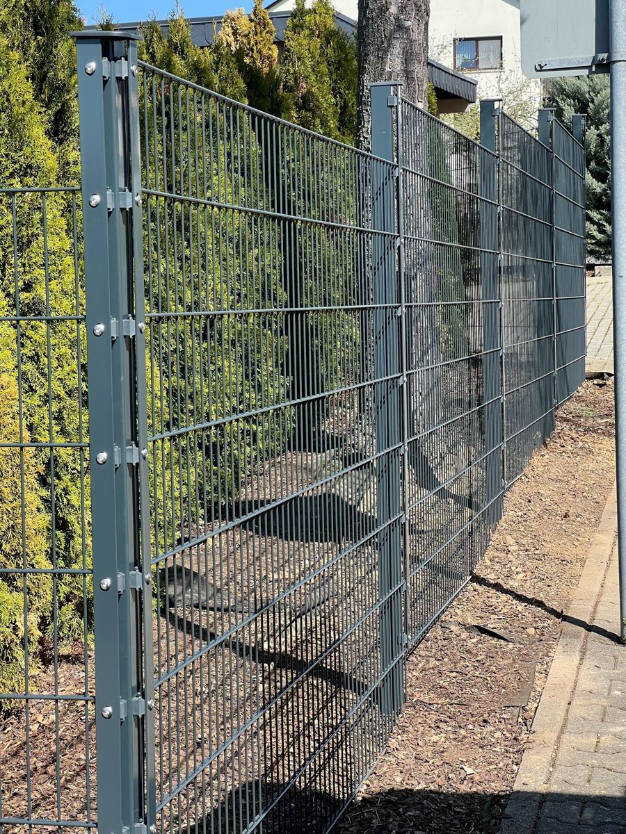 Grauer Maschendrahtzaun neben Grünflächen in einem Wohngebiet.