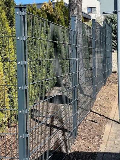 Grauer Maschendrahtzaun neben Grünflächen in einem Wohngebiet.
