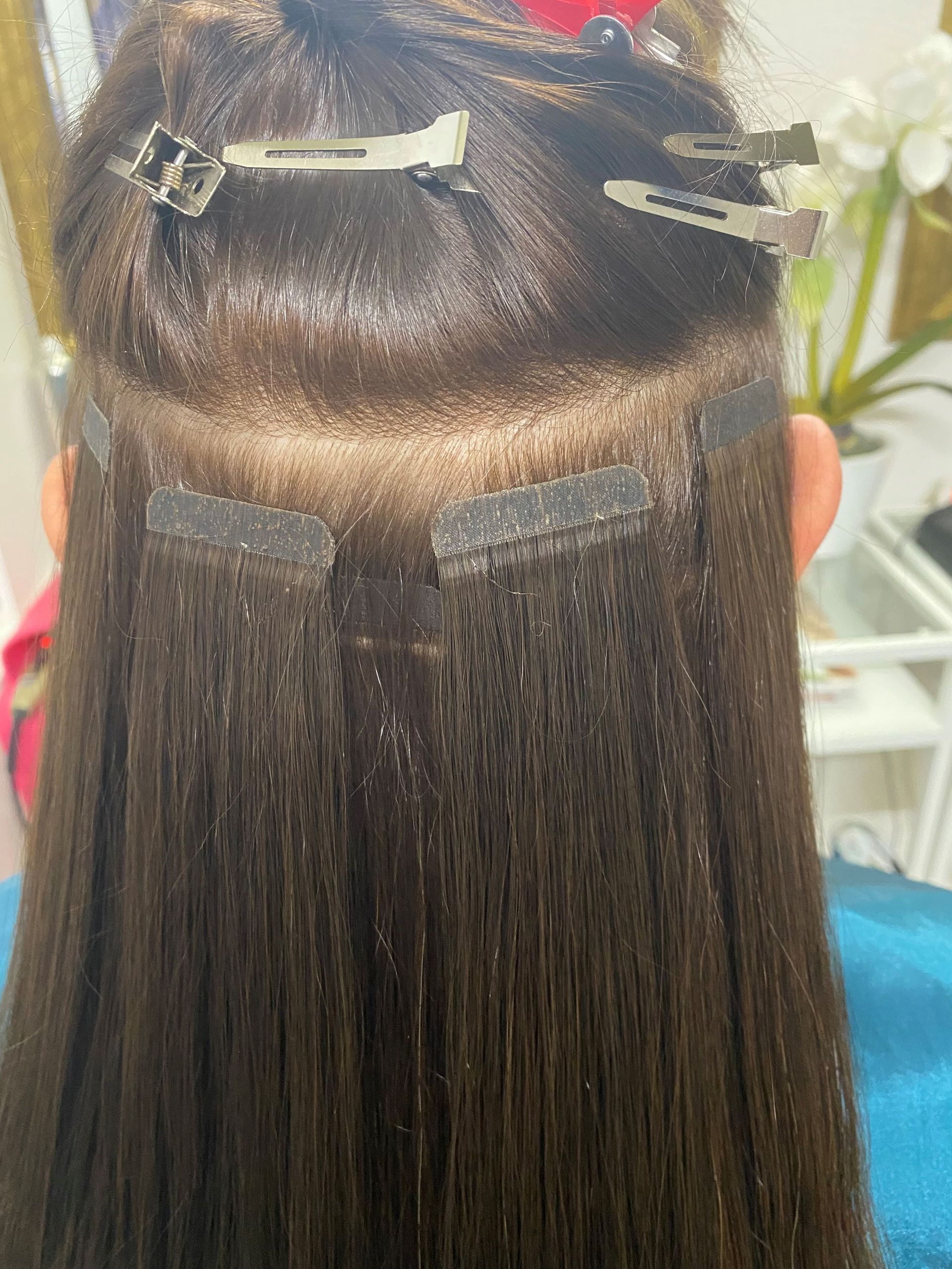 Anbringen von Haarverlängerungen; dunkelbraunes Haar mit sichtbaren Befestigungsstreifen und Clips.