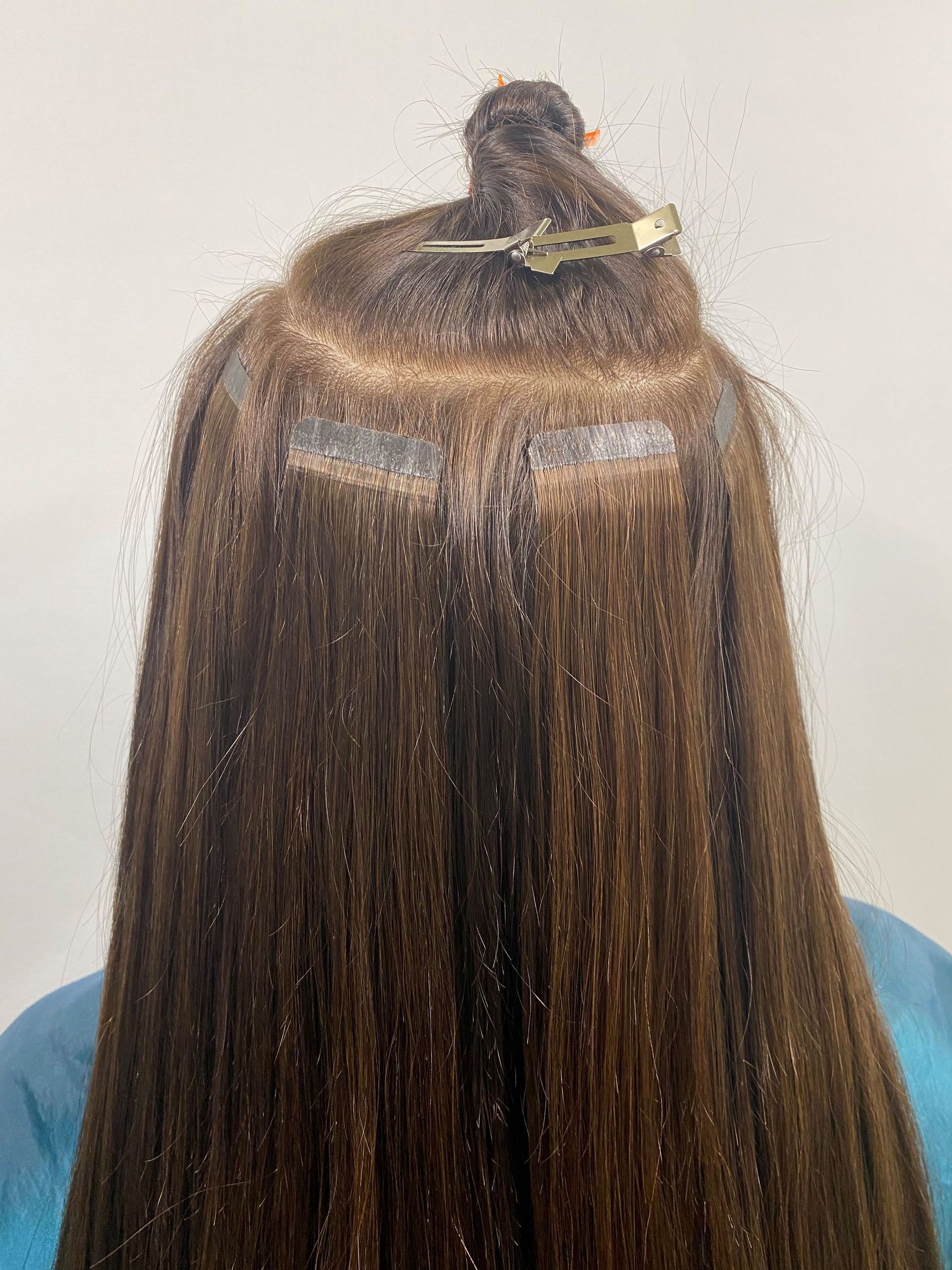 Anbringen von Haarverlängerungen. Zeigt den Vorgang mit Klebeband und Klammer, die den oberen Teil festhalten. Braunes Haar.