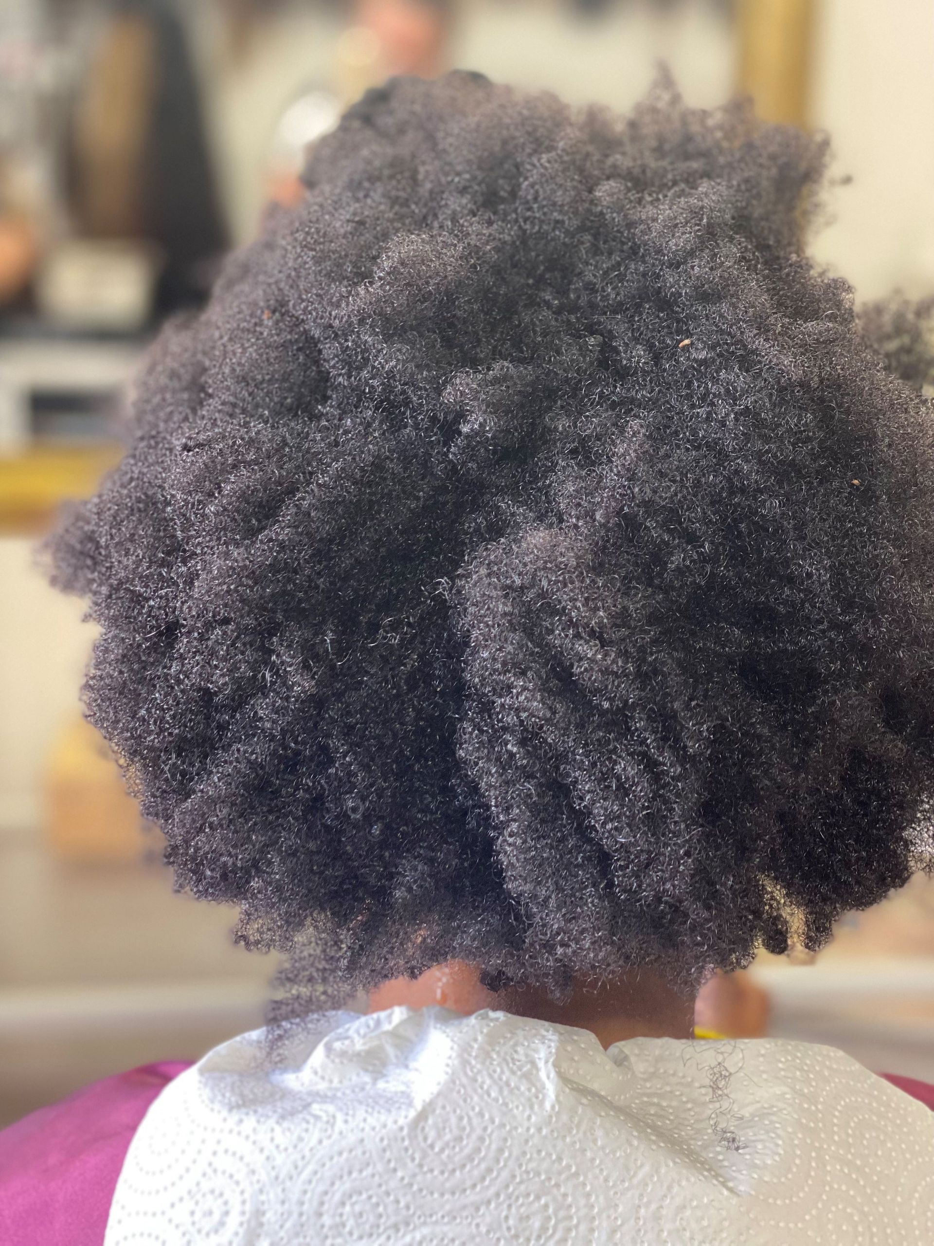 Rückansicht des strukturierten, dunklen Haars einer Person in einem Salon, das mit einem glänzenden Produkt bedeckt ist.