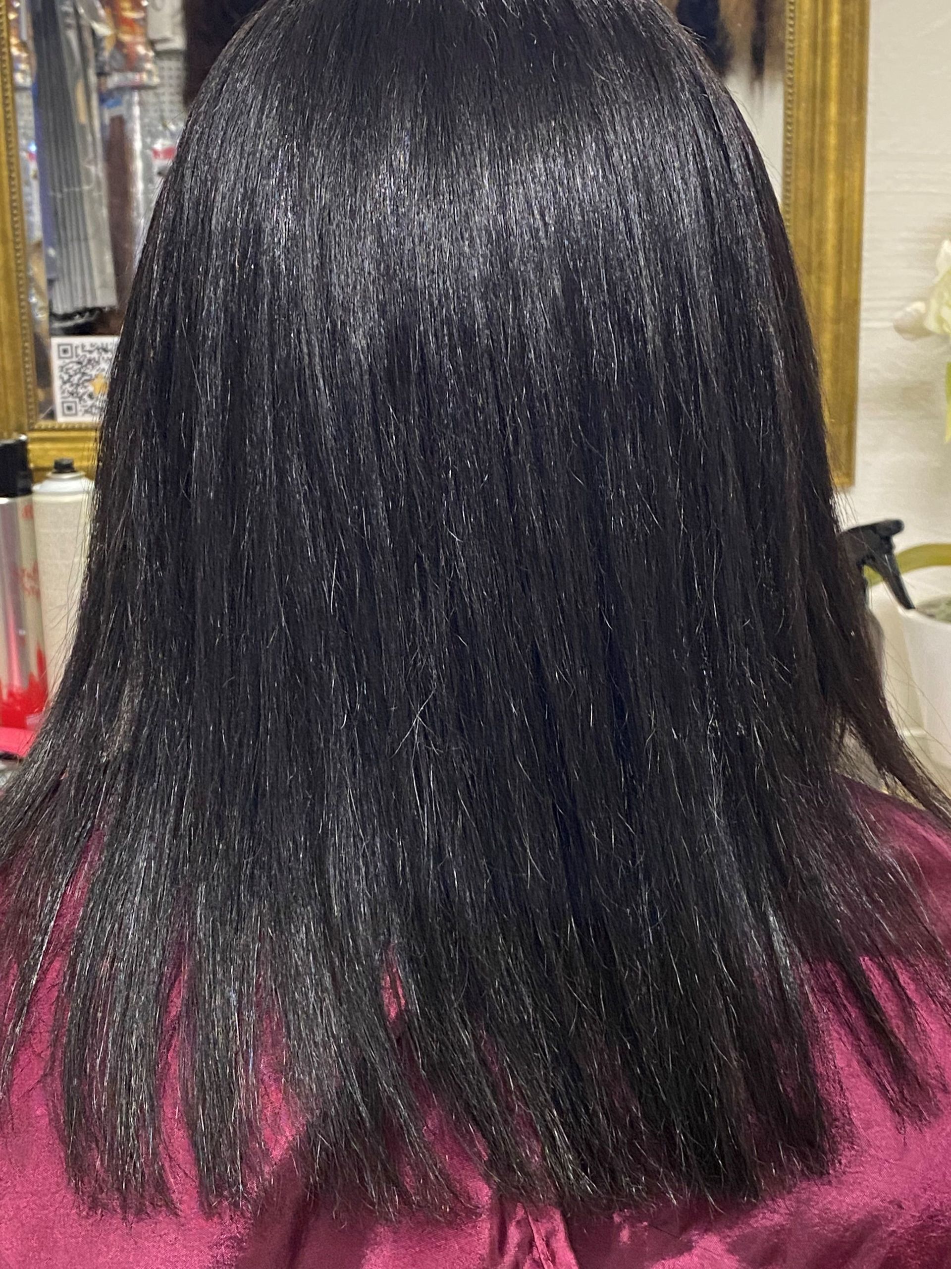 Rückansicht von geglättetem, glänzendem schwarzem Haar mit stumpfem Schnitt; die Person trägt ein burgunderfarbenes Hemd.