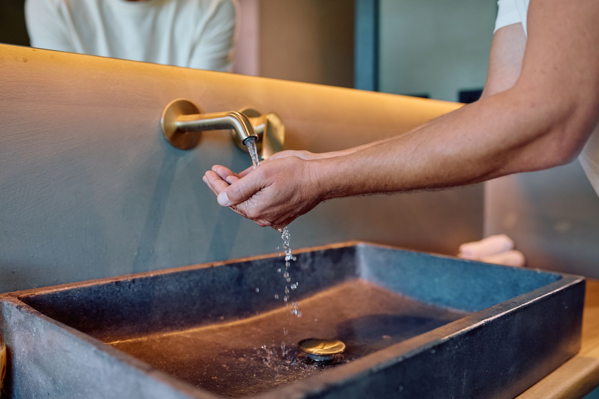 Une personne se lave les mains sous un robinet placé au-dessus d'un lavabo.