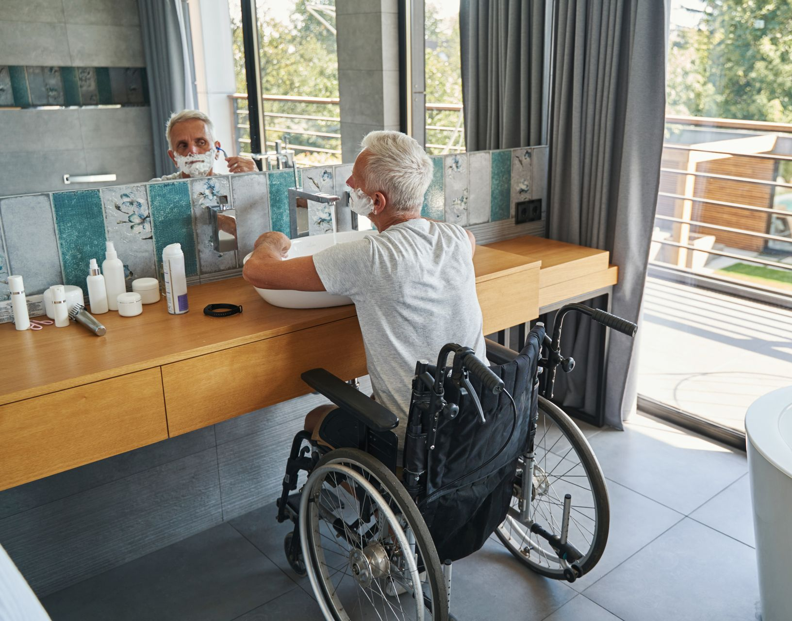 Une personne en fauteuil roulant qui se rase la barbe au-dessus d'un lavabo.