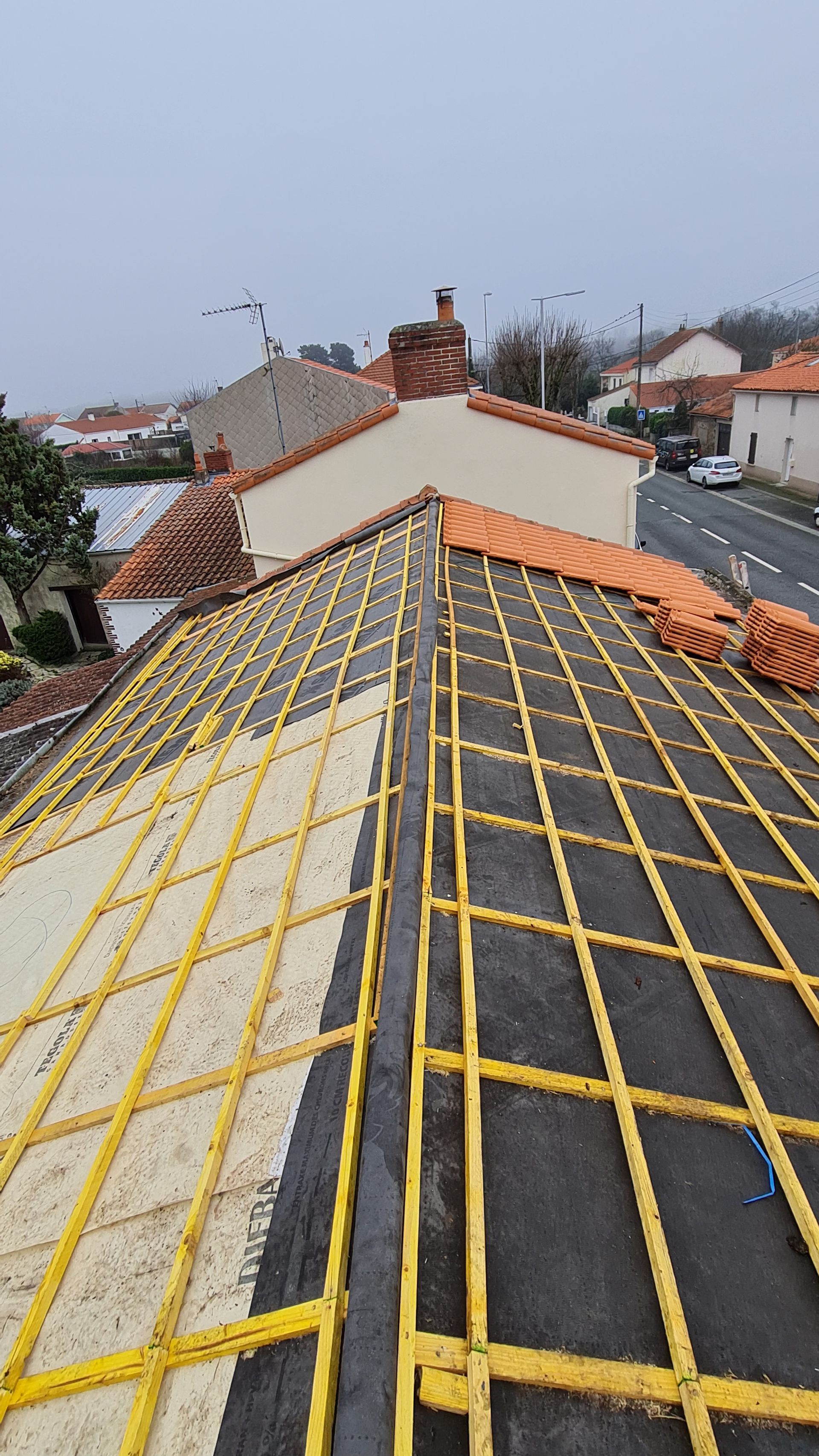 Photo de l'installation des tuiles sur les tasseaux d'une charpente en bois