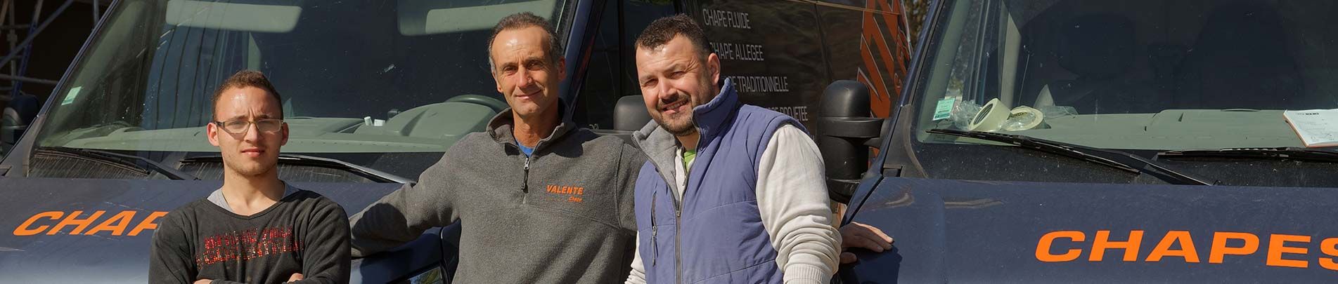 Trois personnes se tiennent devant une camionnette sombre avec des inscriptions orange.