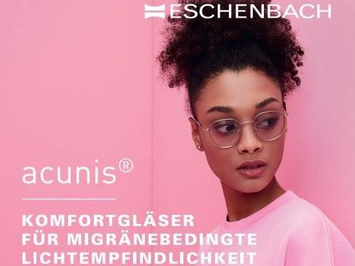 Eine Frau mit Brille steht vor einem rosa Hintergrund.