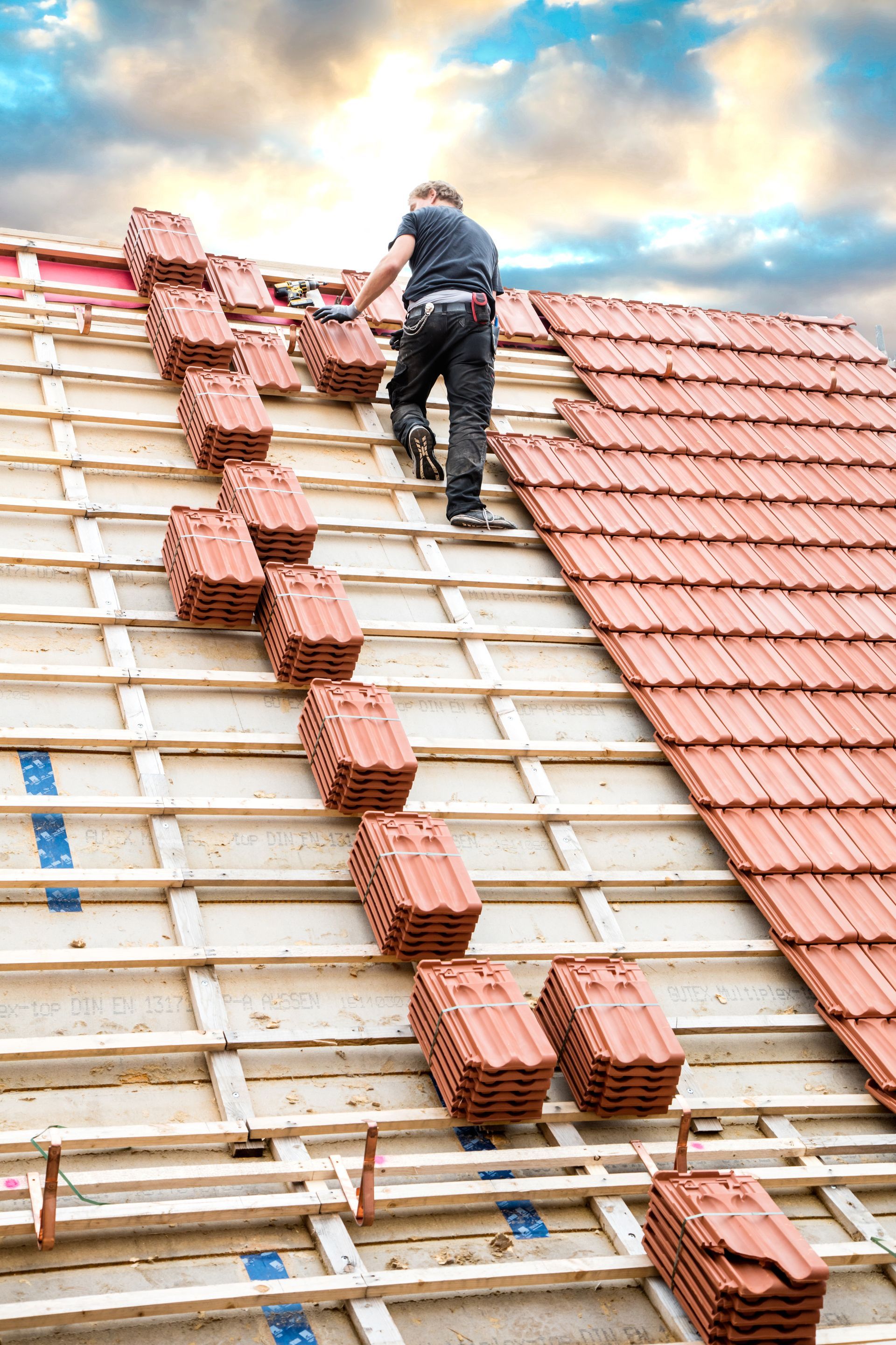 Un couvreur pose des tuiles en terre cuite rouge sur le toit d'une maison. Ciel bleu en arrière-plan.