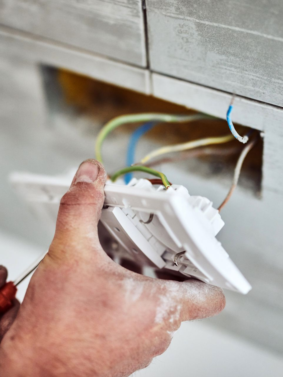 Installation manuelle d'une prise électrique blanche dans un mur, fils apparents.