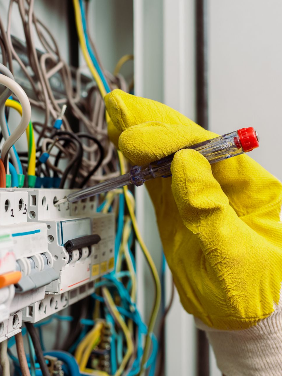Main gantée de jaune testant le câblage électrique avec un tournevis.