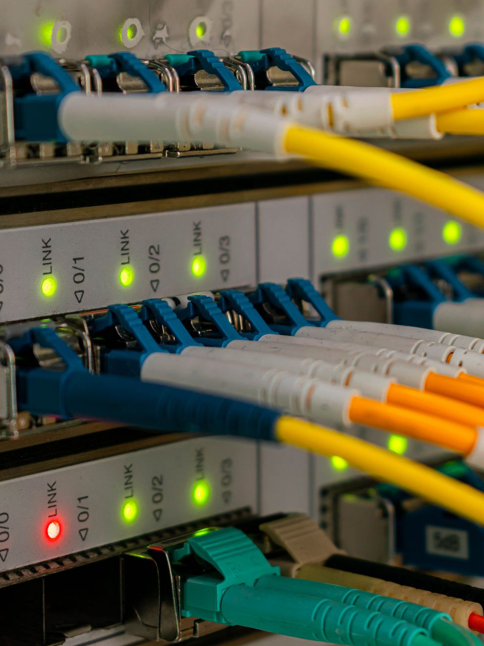 Baie de serveurs réseau avec câbles colorés branchés, lumières allumées.
