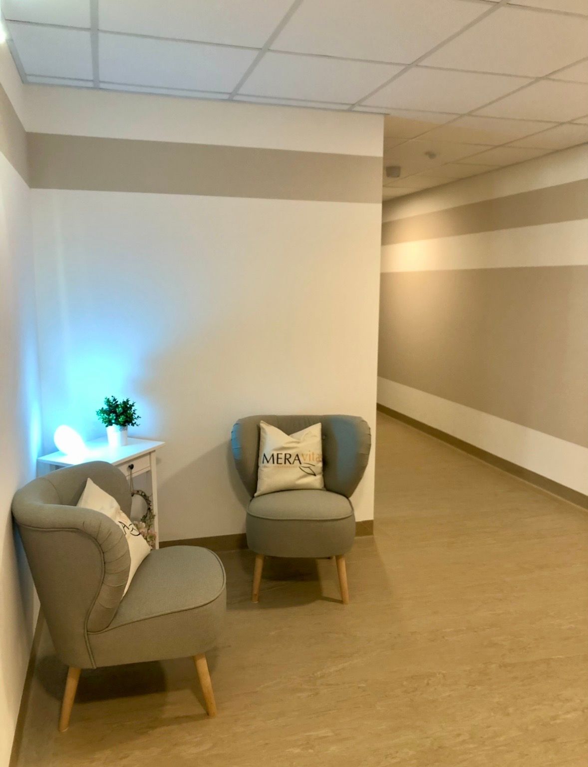 Gemütliche Sitzecke im Flur mit zwei grauen Sesseln, Deko-Kissen und einer sanften Beleuchtung.