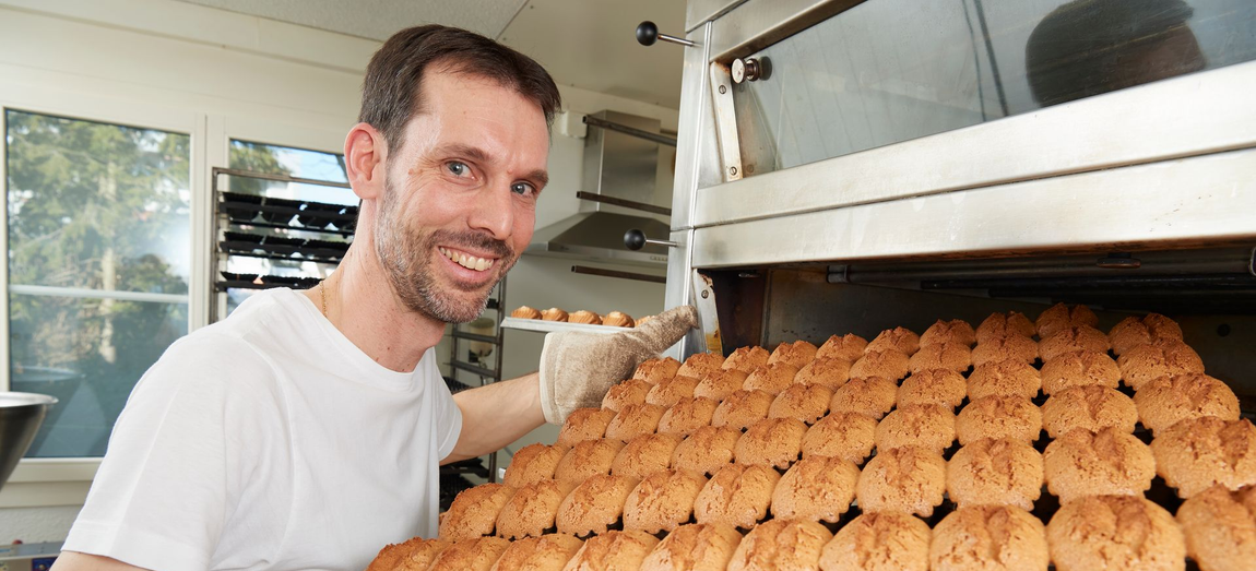Mann mit duzenden Gebäckstücken vor dem Ofen