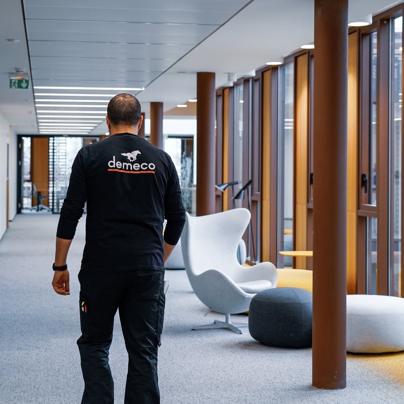 Personne marchant dans un couloir de bureau moderne, avec des chaises blanches et des piliers en bois