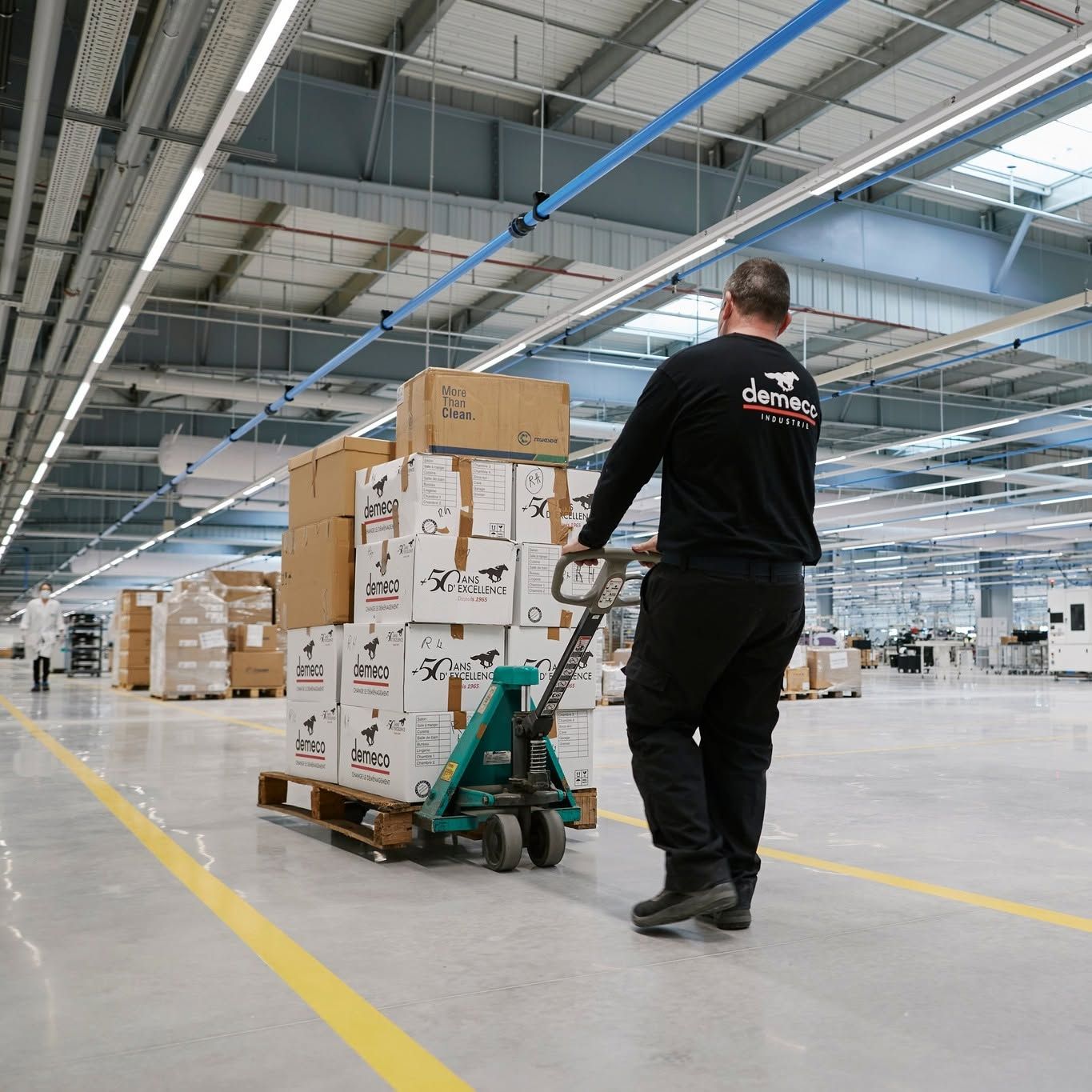 Un employé manœuvre un transpalette pour déplacer des cartons empilés dans un grand entrepôt