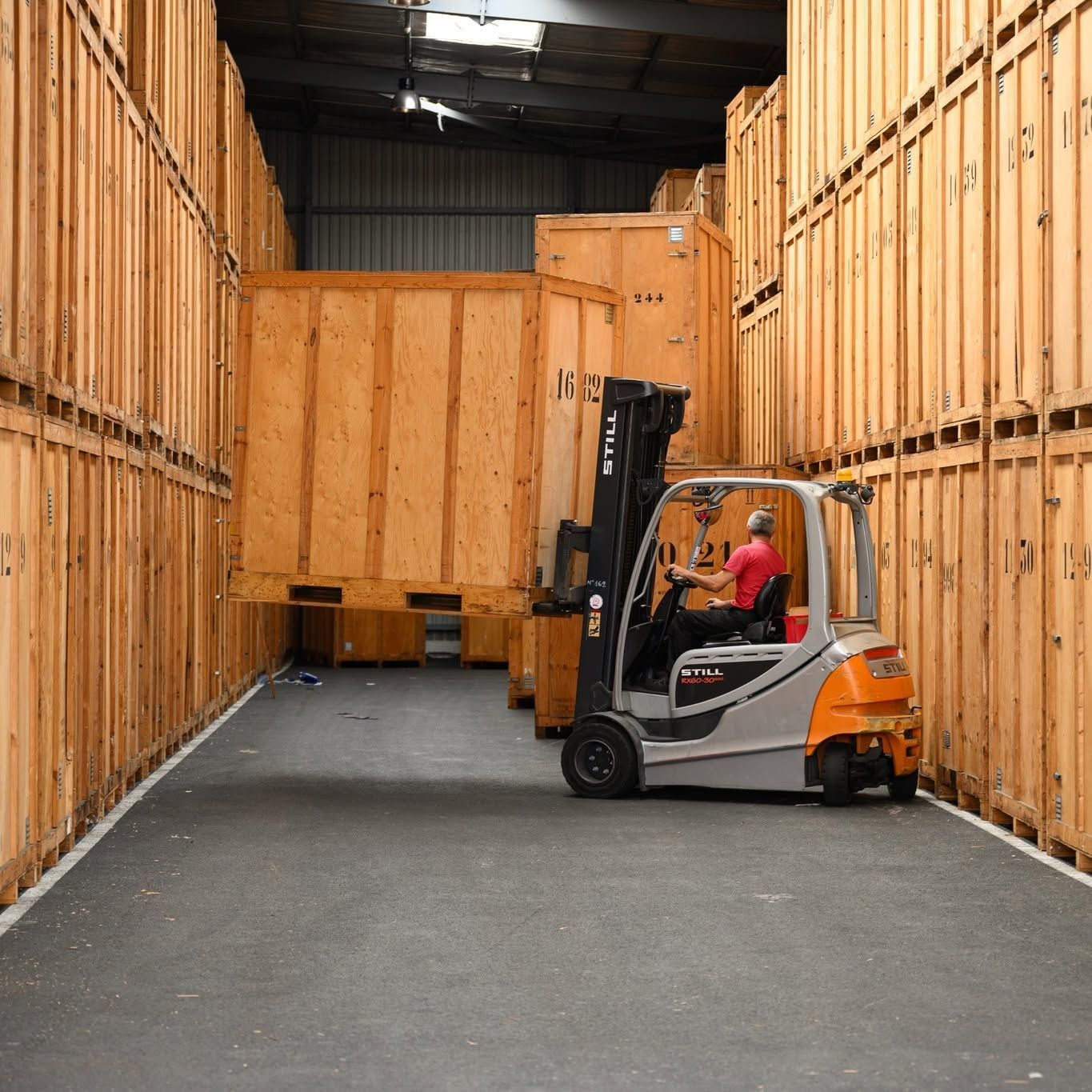 Un chariot élévateur dans une allée d’entrepôt bordée de hautes parois de stockage en bois, conduit par un ouvrier.
