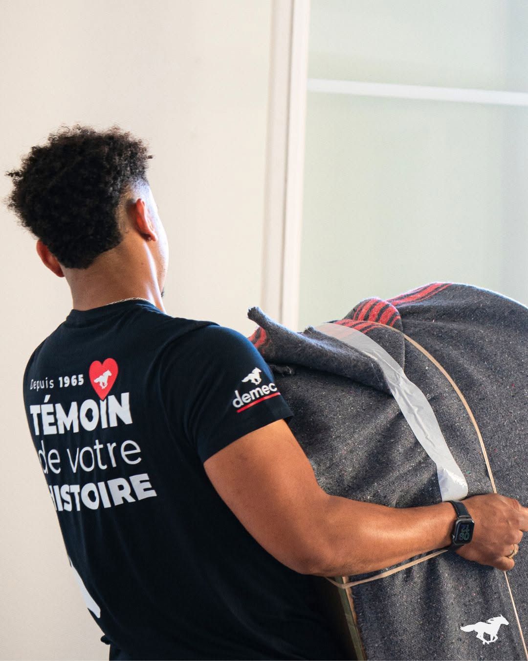 Homme transportant une couverture pliée à l’intérieur, portant un t-shirt noir avec du texte blanc et un logo de cœur rouge