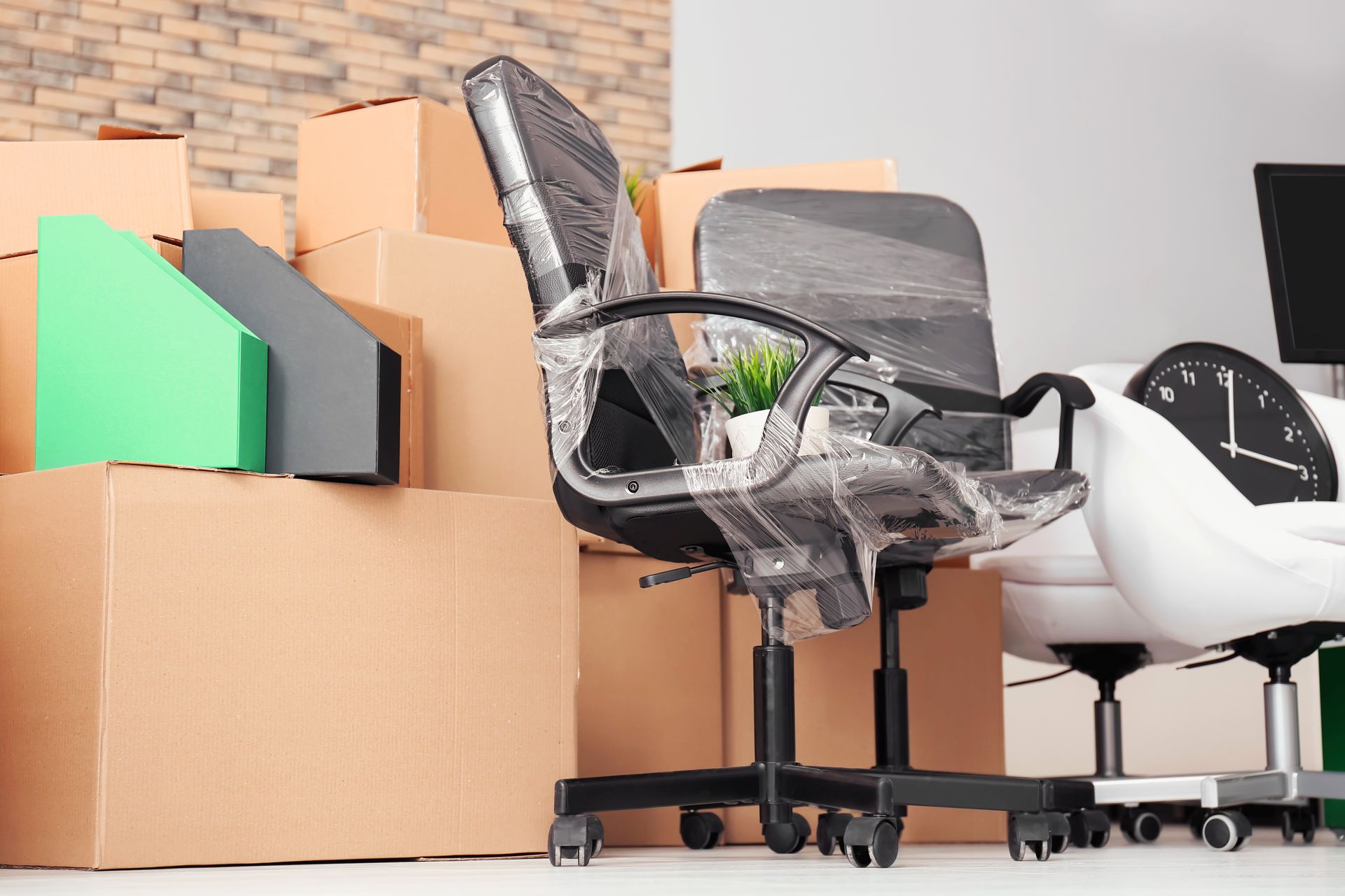 Des cartons de déménagement empilés à côté d’une chaise de bureau en résille noire et d’une chaise blanche, dans une pièce