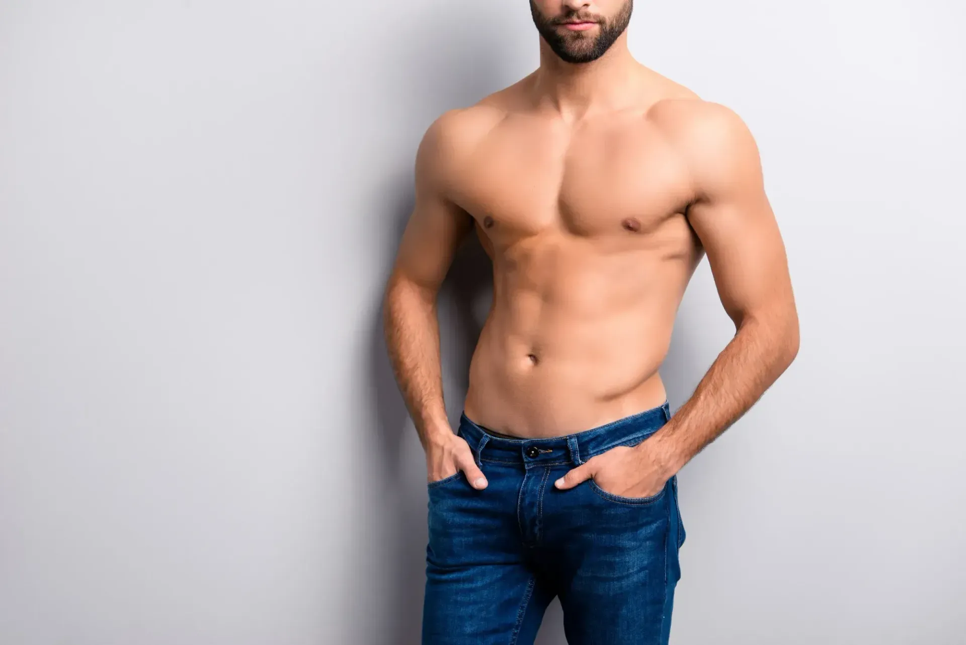 Hombre, torso desnudo, en jeans, manos en los bolsillos, sobre un fondo gris.