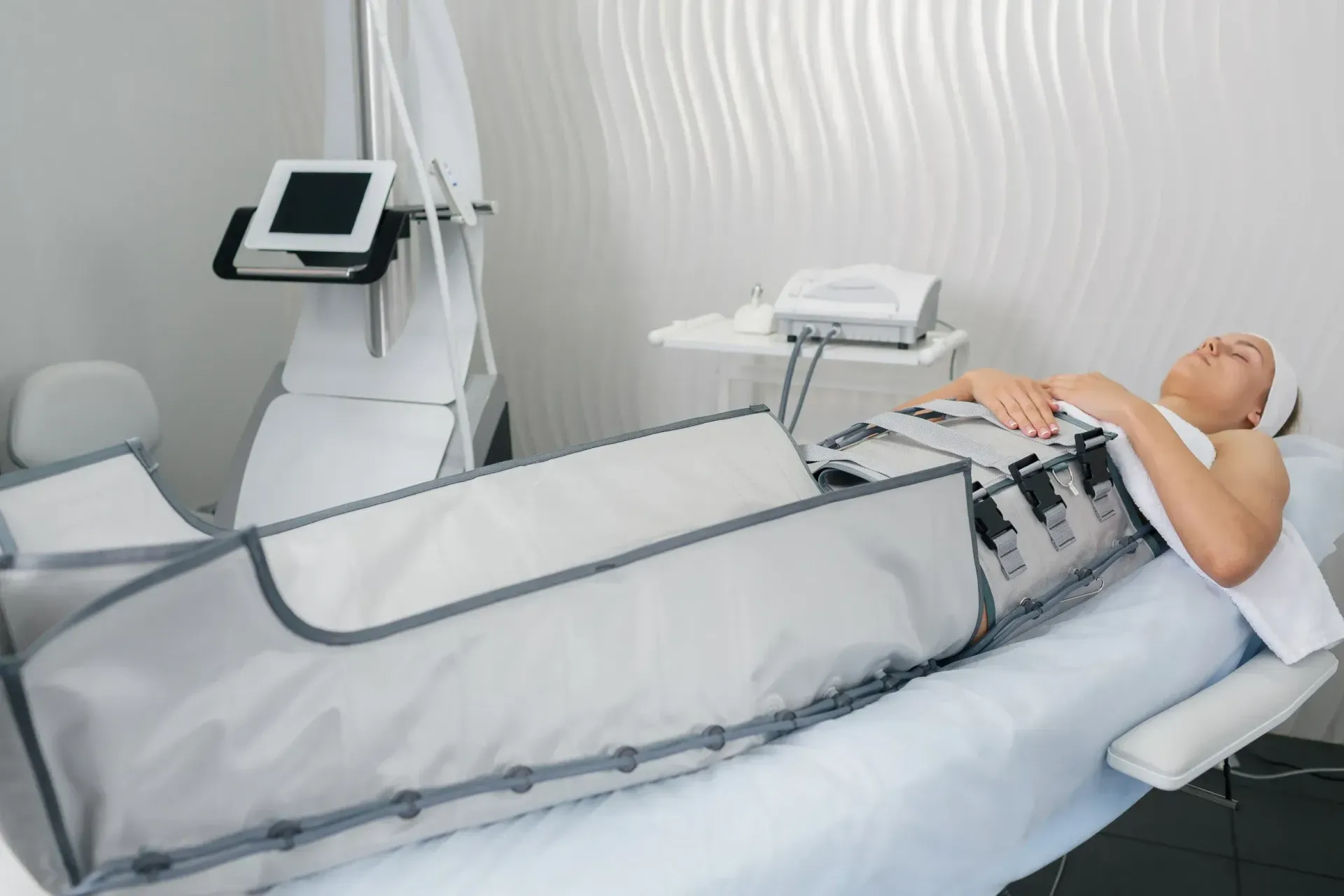 Mujer recibe tratamiento de drenaje linfático en un spa médico, acostada en una cama con un traje de compresión.
