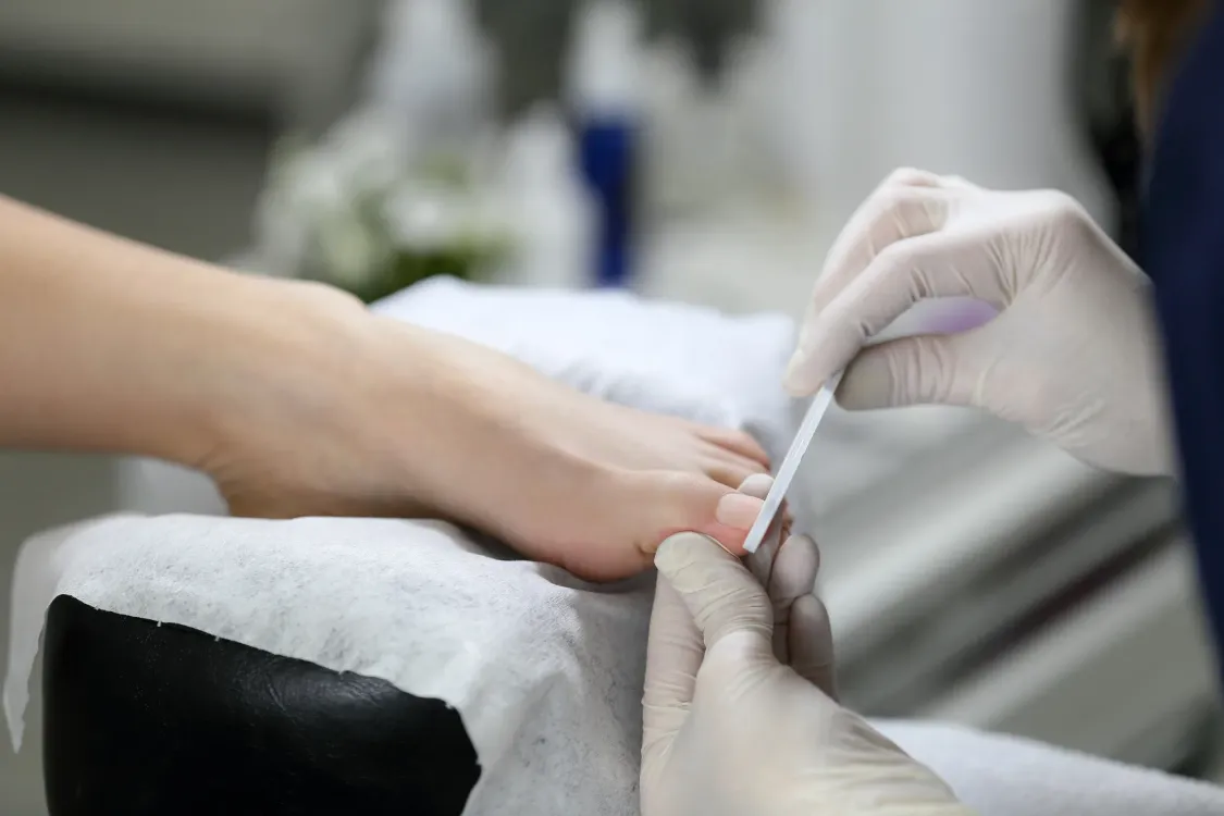 Una persona haciéndose la pedicura; el técnico lima las uñas de los pies. Guantes blancos, primer plano.