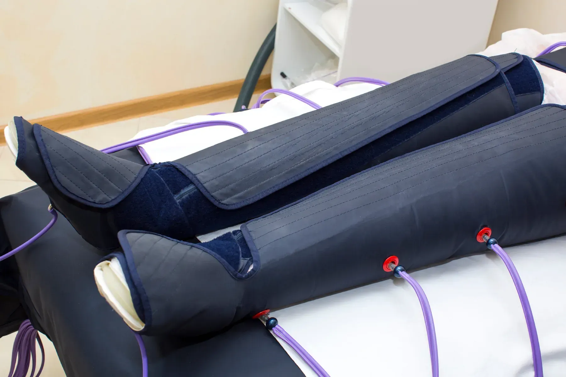 Piernas con mangas de compresión negras conectadas a tubos morados sobre una cama blanca.