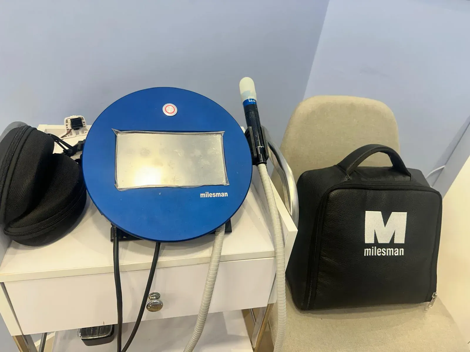 Dispositivo médico azul con varilla adjunta y estuche de transporte sobre una mesa blanca.