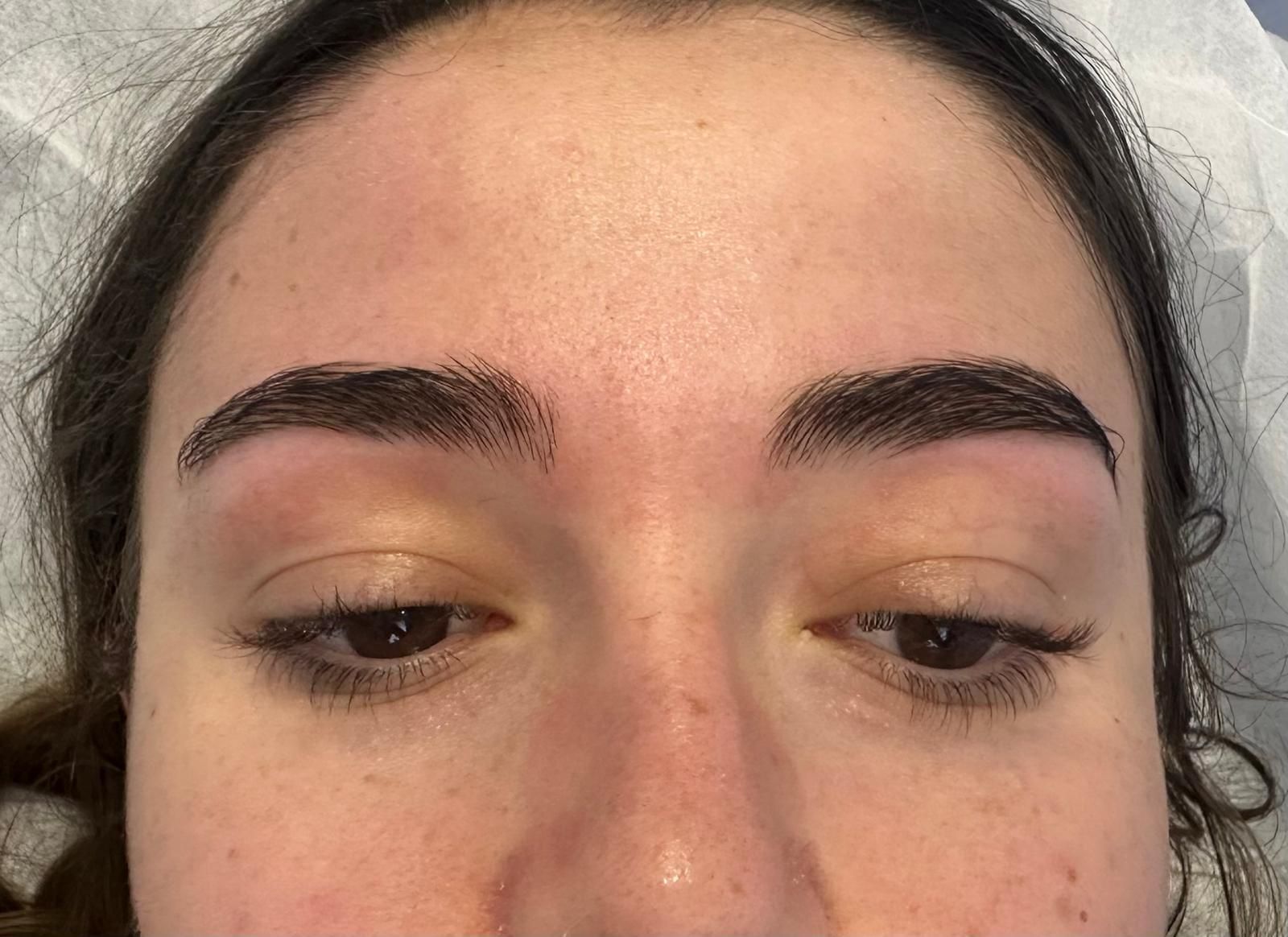 Primer plano del rostro de una persona con cejas oscuras, recién tatuadas y rellenas.