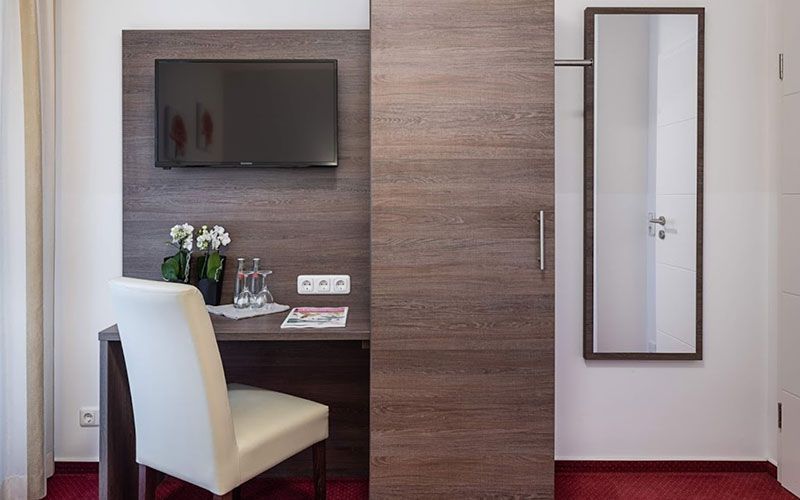 Ein Hotelzimmer mit Schreibtisch, Stuhl, Fernseher und Spiegel.