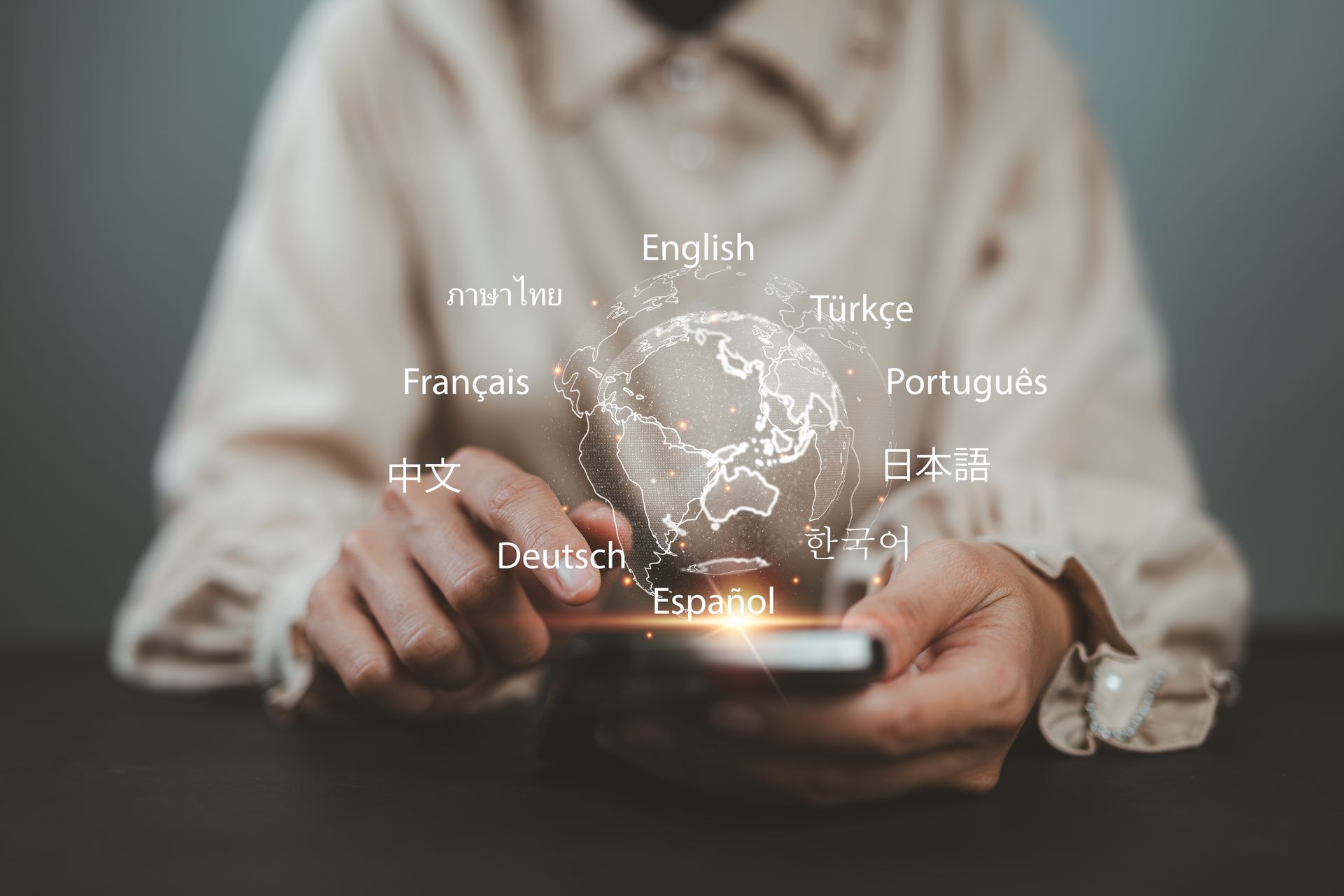 Des mains tenant un smartphone avec un globe holographique lumineux entouré d'étiquettes textuelles en différentes langues.