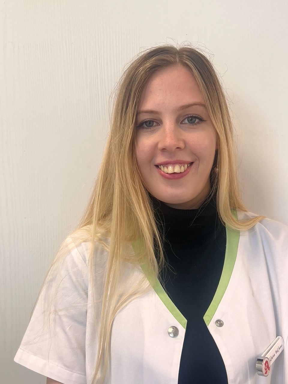 Blonde Frau in Arztuniform lächelt in die Kamera.