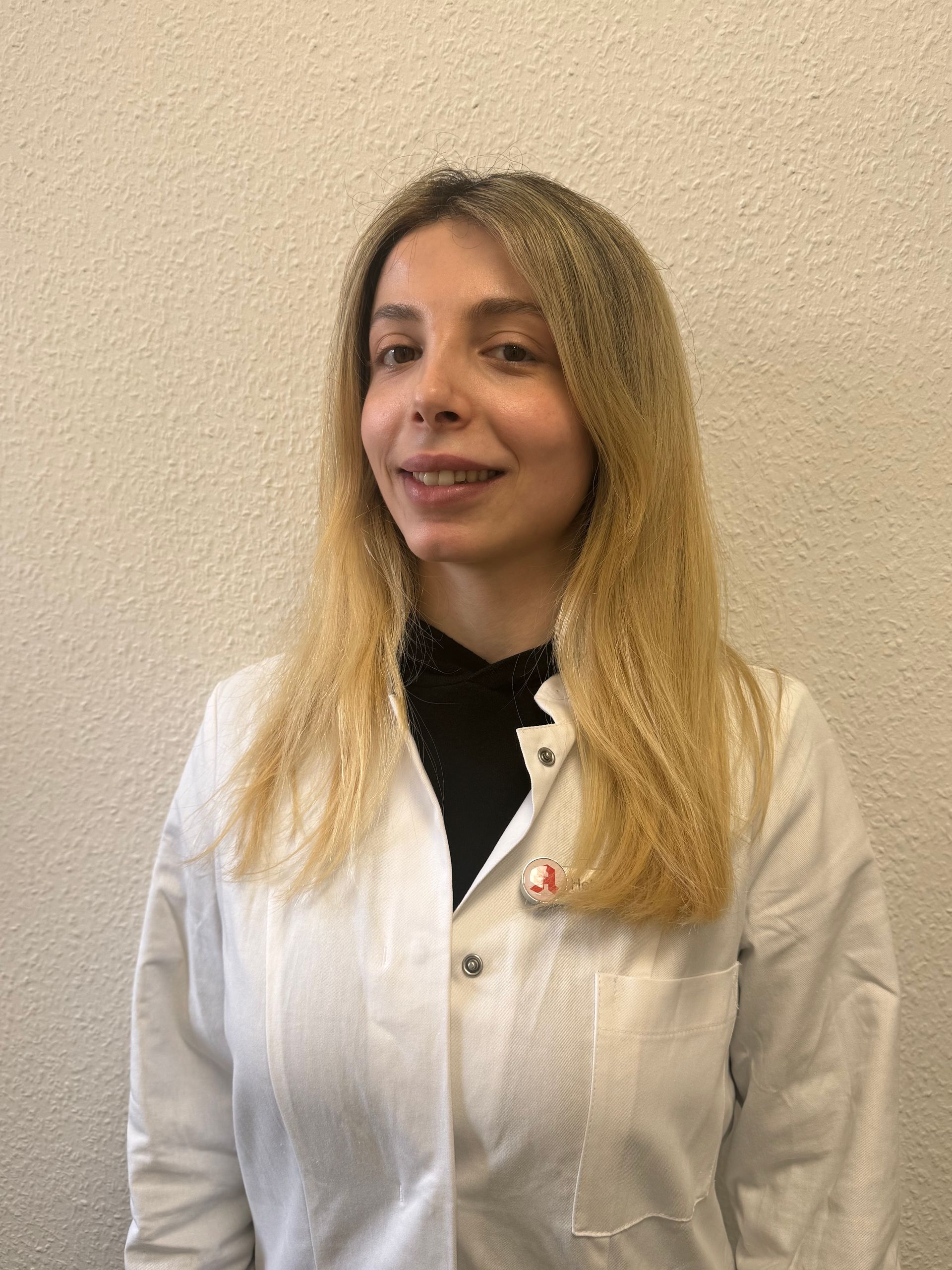 Frau in weißer Uniform mit Namensschild, lächelt in die Kamera.