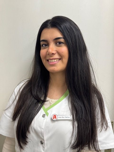 Frau in weißer Uniform mit Namensschild, lächelt in die Kamera.