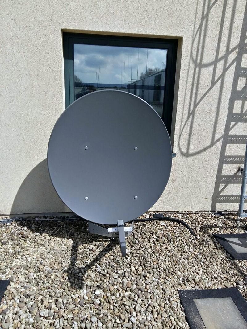 Eine Satellitenschüssel steht auf einem Kieshaufen vor einem Gebäude.