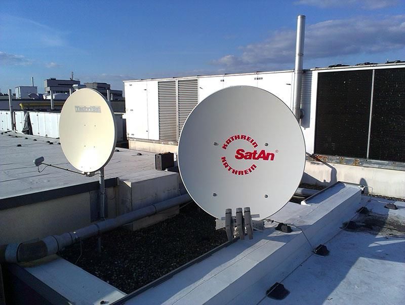 Zwei Satellitenschüsseln auf einem Dach mit der Aufschrift „Satan“