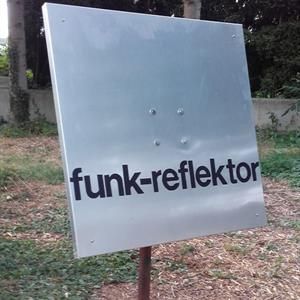 Im Gras sitzt ein Schild mit der Aufschrift „Funk-Reflektor“.