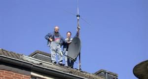 Zwei Männer stehen auf einem Dach und halten eine Satellitenschüssel.