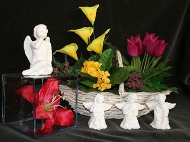 Composition florale dans un panier, agrémentée de figurines d'anges. On y trouve des lys, des tulipes et des arums.