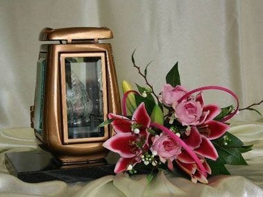 Lanterne commémorative en bronze et composition florale sur une surface drapée de blanc.