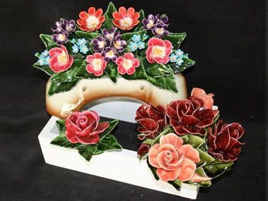 Composition florale en céramique blanche et beige, avec des fleurs rouges, roses et violettes.