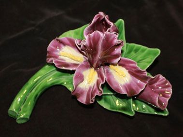 Fleur d'iris en céramique violette et jaune à feuilles vertes sur fond sombre.