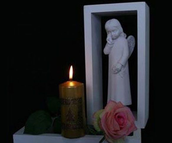 Flamme d'une bougie près d'une statue d'ange, d'une rose rose et d'une structure encadrée de blanc.