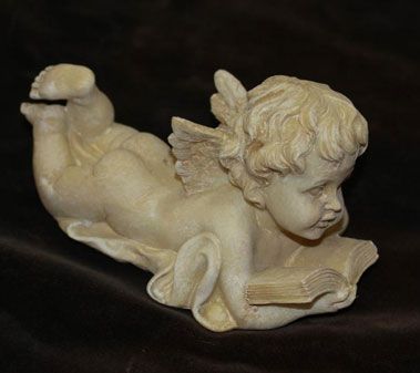 Sculpture d'un chérubin couché sur le ventre, lisant un livre. Couleur beige, petites ailes.