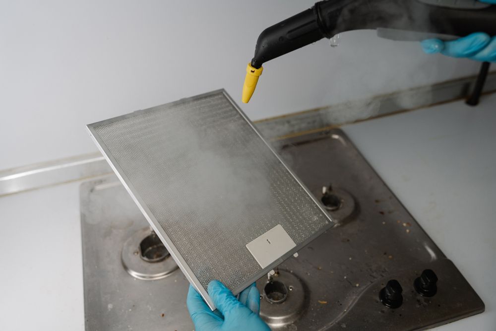 Limpieza con vapor del filtro de ventilación de una cocina encima de la estufa.